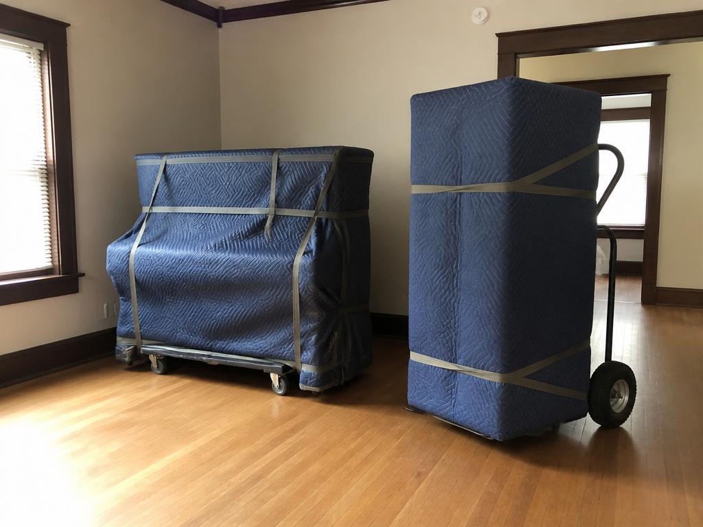 Upright piano and large safe wrapped in moving blankets on a hand truck